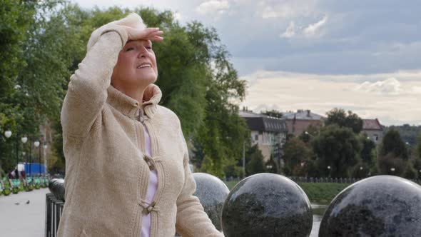 Attractive Elderly Woman Puts Hand to Forehead Covering Eyes From Bright Sunlight Peering Into alt