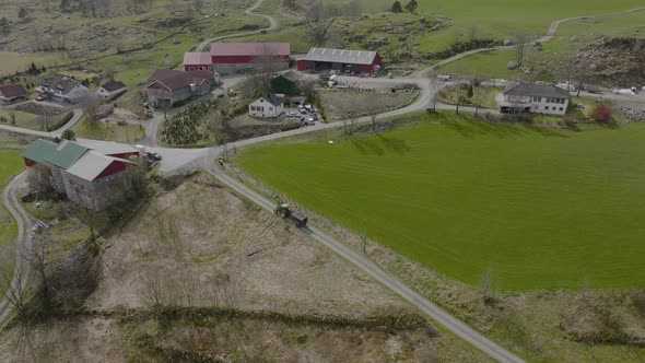 Aerial drone flies over tractor, green field, farms, barns, Norway. alt