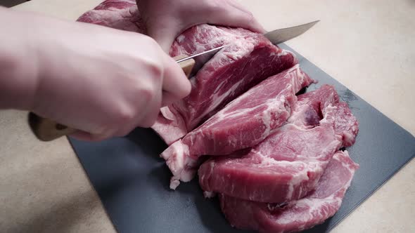 cutting raw meat on a cutting board. close-up of hands with knife and pork.