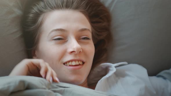 Young Woman with Long Hair Wakes Up, Gets Up on Bed and Stretches in Morning Sun Light alt