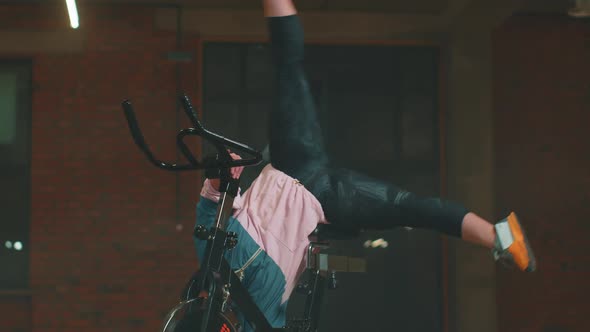 Athletic Woman Makes Twine Training Routine on Spinning Stationary Bike in Gym Stretching Exercises alt