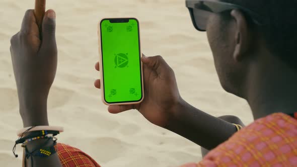 African Maasai Male Hand Holding a Smartphone with Green Screen and Swiping in the Front of Desert