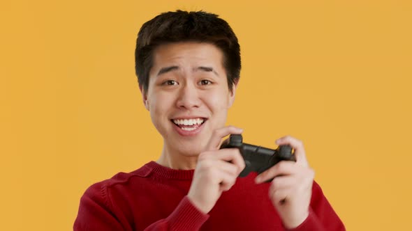 Joyful Asian Guy Playing Videogame Celebrating Victory Over Yellow Background alt