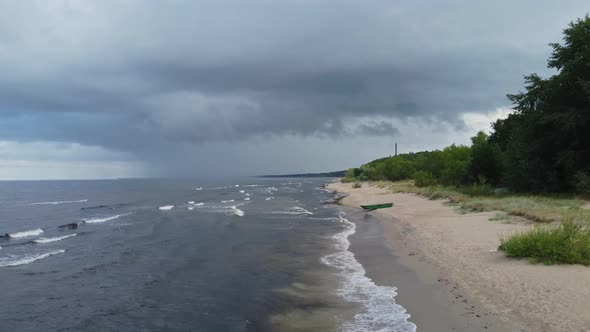 drone flight along the beach and sea with rain clouds. Coastline perspective with rolling waves.