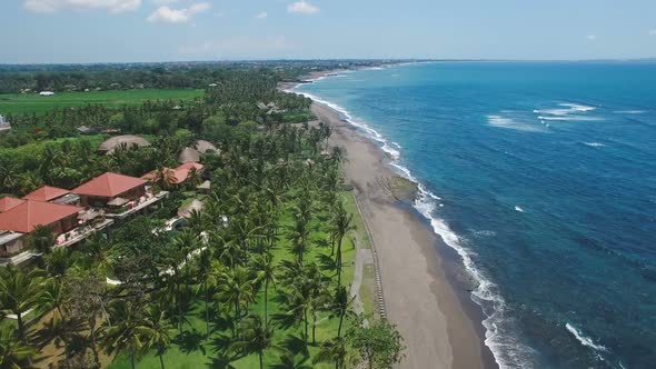 Flying Over Ocean Coast Line with Grey Sand Beach, Azure Ocean and Village Buildings alt