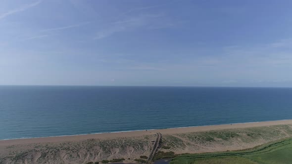 Aerial tracking out to gorgeous blue sky and sea over a pebble beach with a lake immediately in the alt