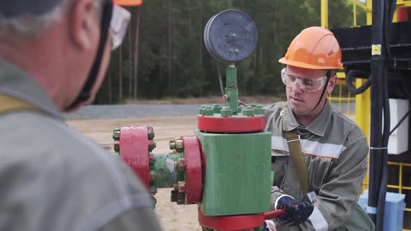 Oilman in Orange Helmet and Protective Glass Closing Valve of X-mass Wellhead To Shut Off Well alt