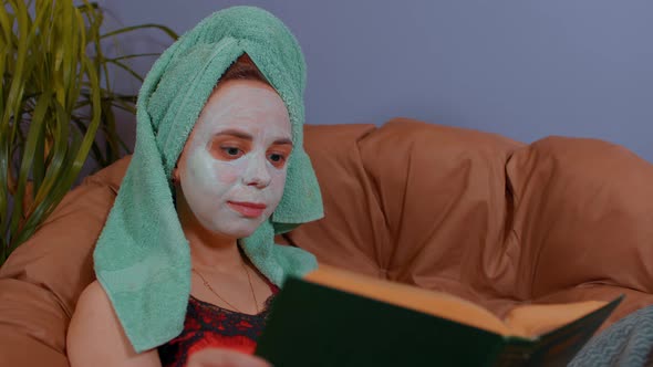 Woman with Towel on Head Mask on Face Sits and Reads Book in Armchair alt