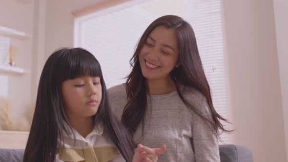 Asian mom teaches daughter to play games and do activities on the sofa on vacation.