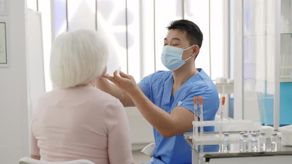 Male Doctor in Protective Mask Taking PCR Test Sample From Throat of Female Retiree Patient and alt
