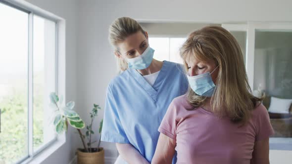 Female health worker assisting senior woman to exercise with dumbbells at home alt