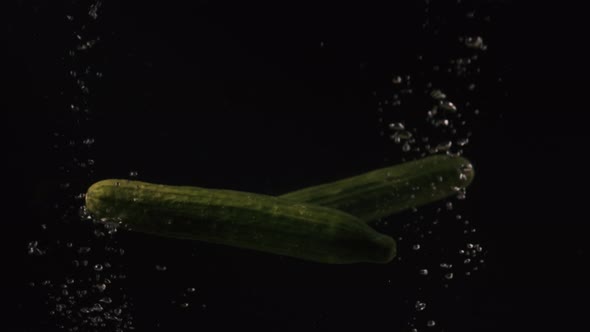 Cucumbers Falling Into Water with Bubbles on Black Background. Vegetables Falling Into Water on alt