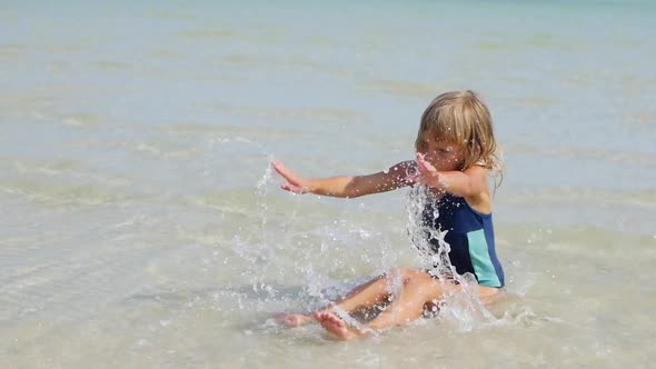 6-Year-old Girl Sits in the Sea in Shallow Water and Splashes Water