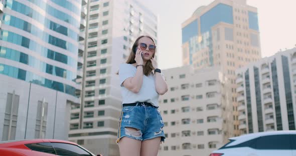 Young Beautiful Woman Talking on the Phone on the Background of Buildings alt
