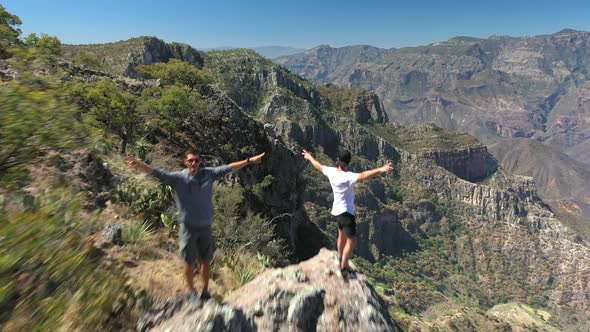 Three men raising arms and overlooking Copper Canyon, Mexico, forward aerial alt