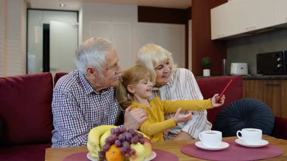 Senior Couple Grandparents with Child Granddaughter Making Selfie Photos Together on Mobile Phone alt