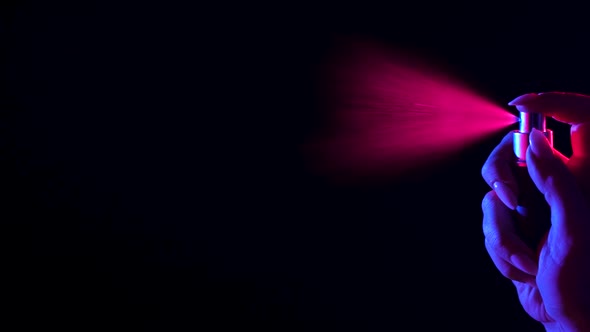 Woman's Hand Finger Sprays Perfume on Black Background with Pink and Blue Neon Light alt