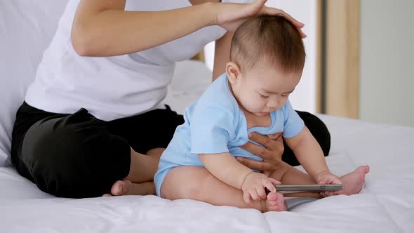 Young mother with her little baby sitting on bed at home. alt