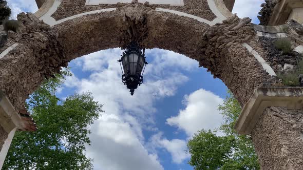 Look up of arch with lamp agains blue and cloudy sky. Beautiful architectural details alt