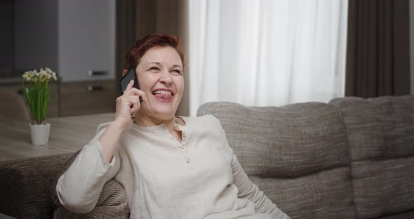 Funny Mature Woman Gossiping with Friend on Smartphone alt