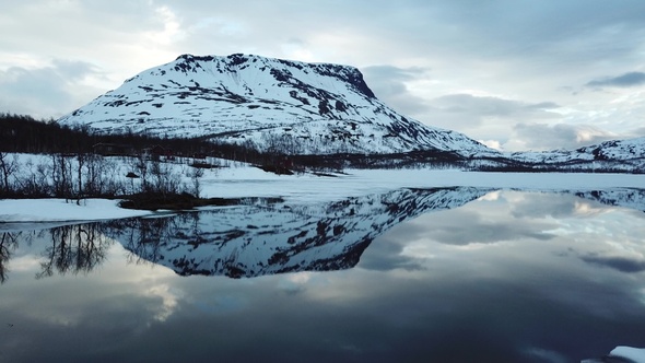 Winter Norwegian landscape with snowy mountains and fjord. Reflection of the mountain in the water. alt
