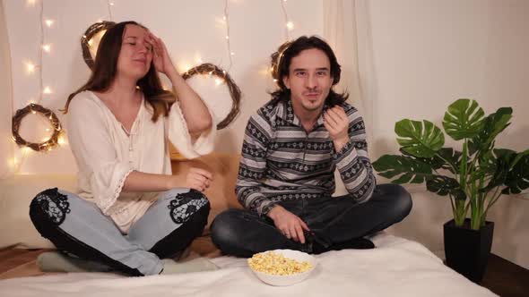 Happy Young People Man and Woman are Watching TV Laughing and Eating Popcorn at Home Enjoying