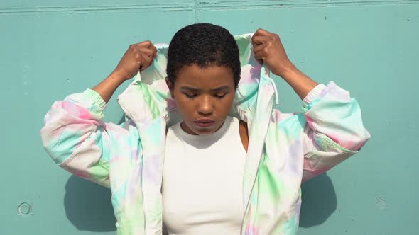 Pretty woman posing in front of blue wall, wearing hood alt