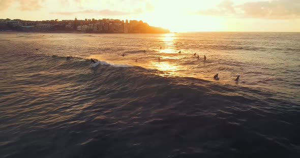Aerial shot of a surfer at Bondi Beach during sunrise catching a wave. alt