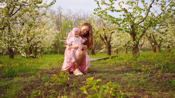 Mother Tying Shoelaces Baby Sit in the Flowering Garden alt