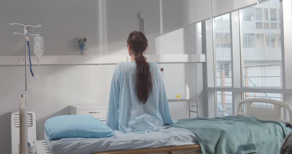 Back View of Young Female Patient Sitting in Hospital Bed alt
