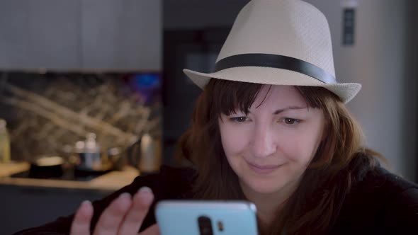 Pretty Woman in a Hat Using the Phone at Home Closeup Writes SMS Surfs the Internet Cinematic Shot
