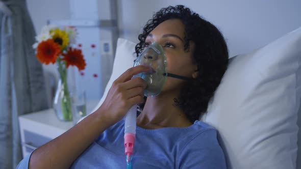 Portrait of african american female patient lying on hospital bed wearing oxygen mask ventilator alt
