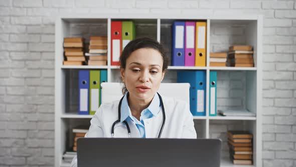 Woman Doctor Sitting at Table in Cabinet of Modern Clinic and Consulting Her Patient By Notebook alt