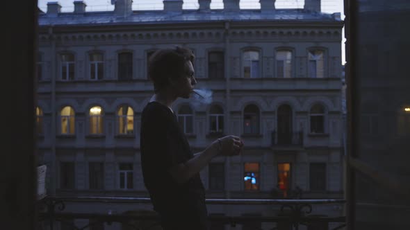 A Young Man Lights a Cigarette on a Balcony Smokes Looks Into the Distance