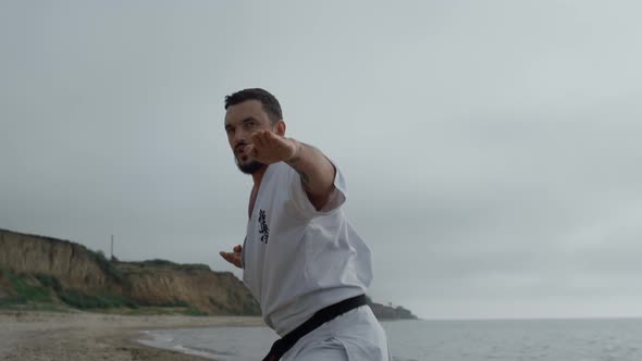 Sportsman Practicing Hands Punches on Gloomy Beach alt