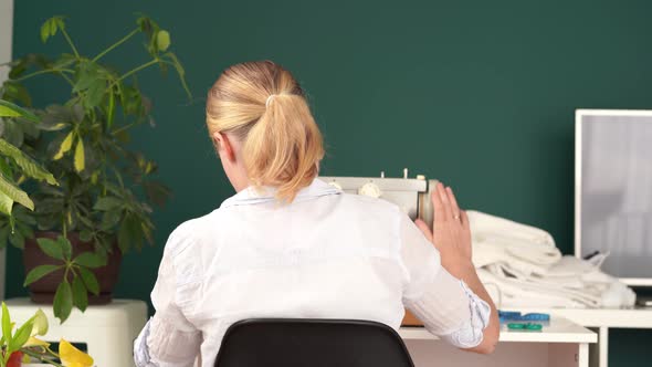 Work at Home. Young Blonde Woman Sews on a Typewriter in a Bright Room