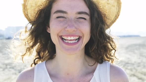 Young joyful woman in white shirt wearing hat smiling at camera on the beach