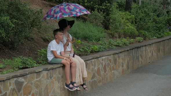 Mother with Her Son Sitting under Umbrella in Park