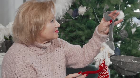 Happy Senior Woman Laughing to the Camera Holding Toy Santa Claus alt