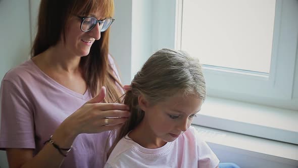 Mother Braids Daughter's Hair By the Window alt
