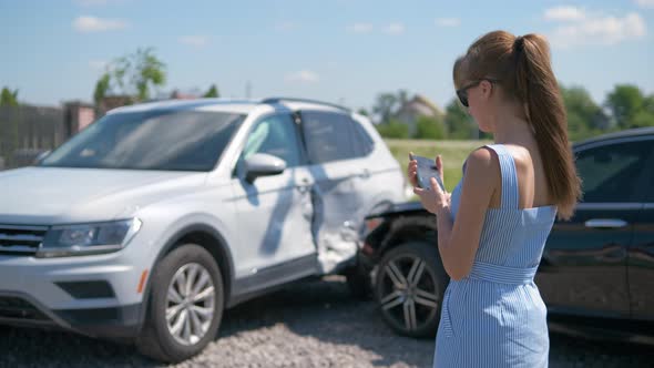 Stressed Driver Taking Picture on Sellphone Camera of Smashed Vehicle Calling for Emergency Service alt