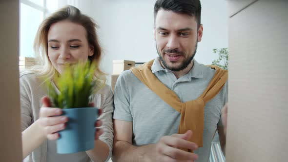 Joyful Man and Woman Unpacking Cardboard Box Looking at Things and Kissing During Relocation alt