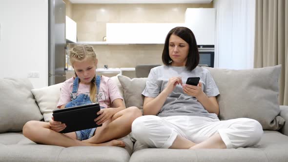 Caucasian Young Mother and Teen Daughter Resting on the Sofa at Home and Using the Tablet Device and