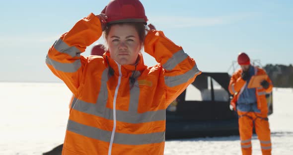 Portrait of Woman Lifesaver Putting on Hardhat Standing on Frozen Lake in Winter alt