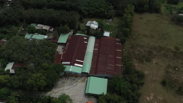 Aerial orbit shot of factory building in Cu Chi, Vietnam with farms, forests on sunny day with blue alt