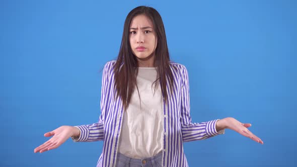 Confused and Indignant Young Asian Woman Stands on the Blue Background alt