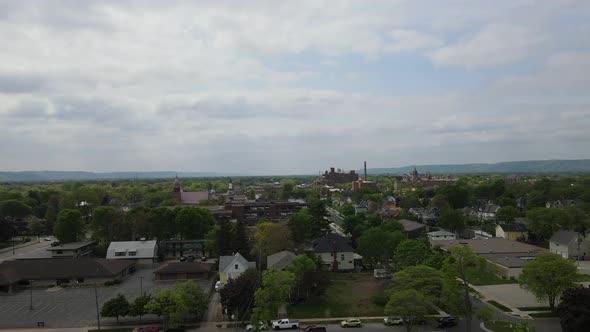 Aerial view over midwest city with tree lined streets, homes, mountains, and hazy sky.