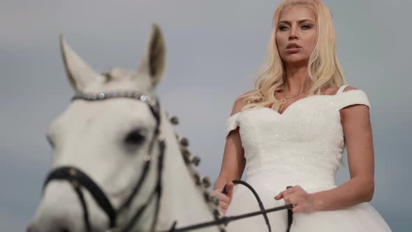 Portrait of a Blonde with Long Hair and in a Fluffy White Dress Riding a Horse alt