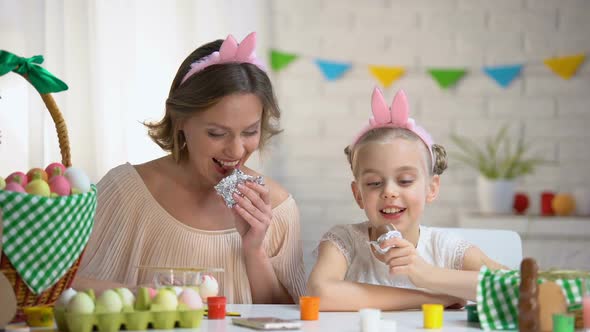 Beautiful Mother and Daughter in Funny Headbands Eating Easter Chocolate Eggs alt