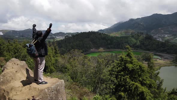 Young man standing on a rock of a cliff and enjoying the view alt